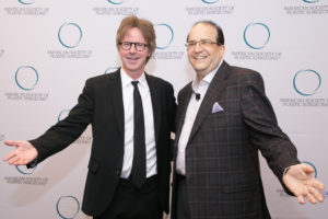 Dr. Glasberg posing and smiling with another man in front of American society of plastic surgeons background